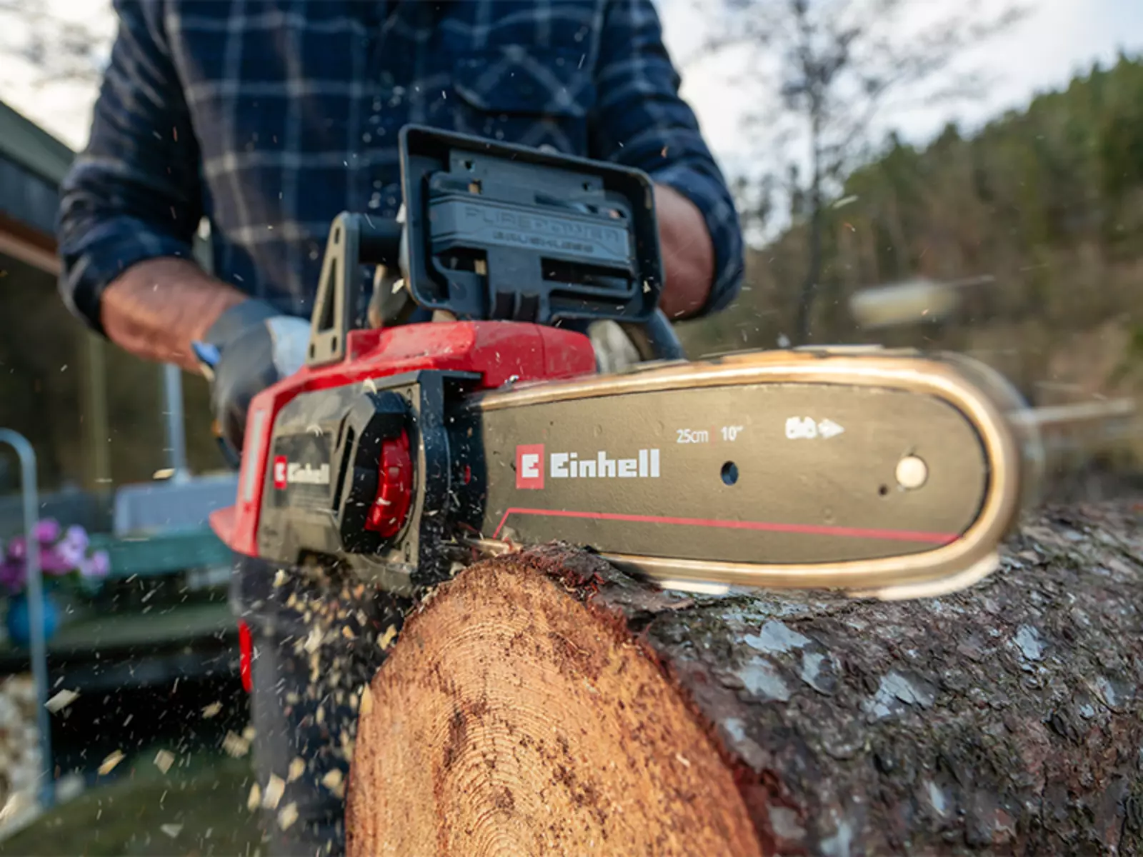 Крупний план акумуляторної бензопили Einhell GE-LC 18/25 Li BL, яка розпилює стовбур дерева, летить деревна тріска.