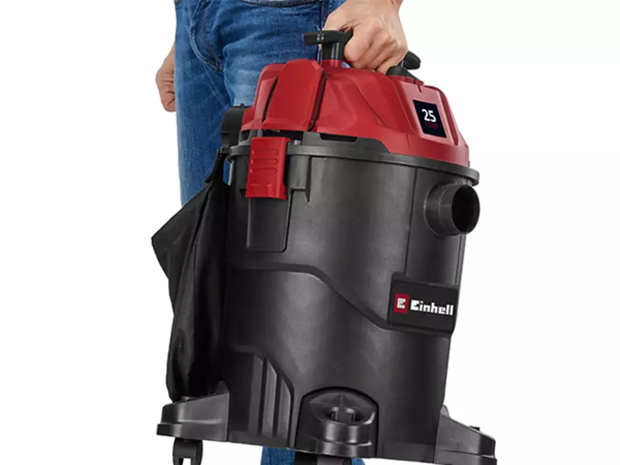 Пользователь несет пылесос Einhell TC-VC 2555 для сухой и влажной уборки за боковую ручку.